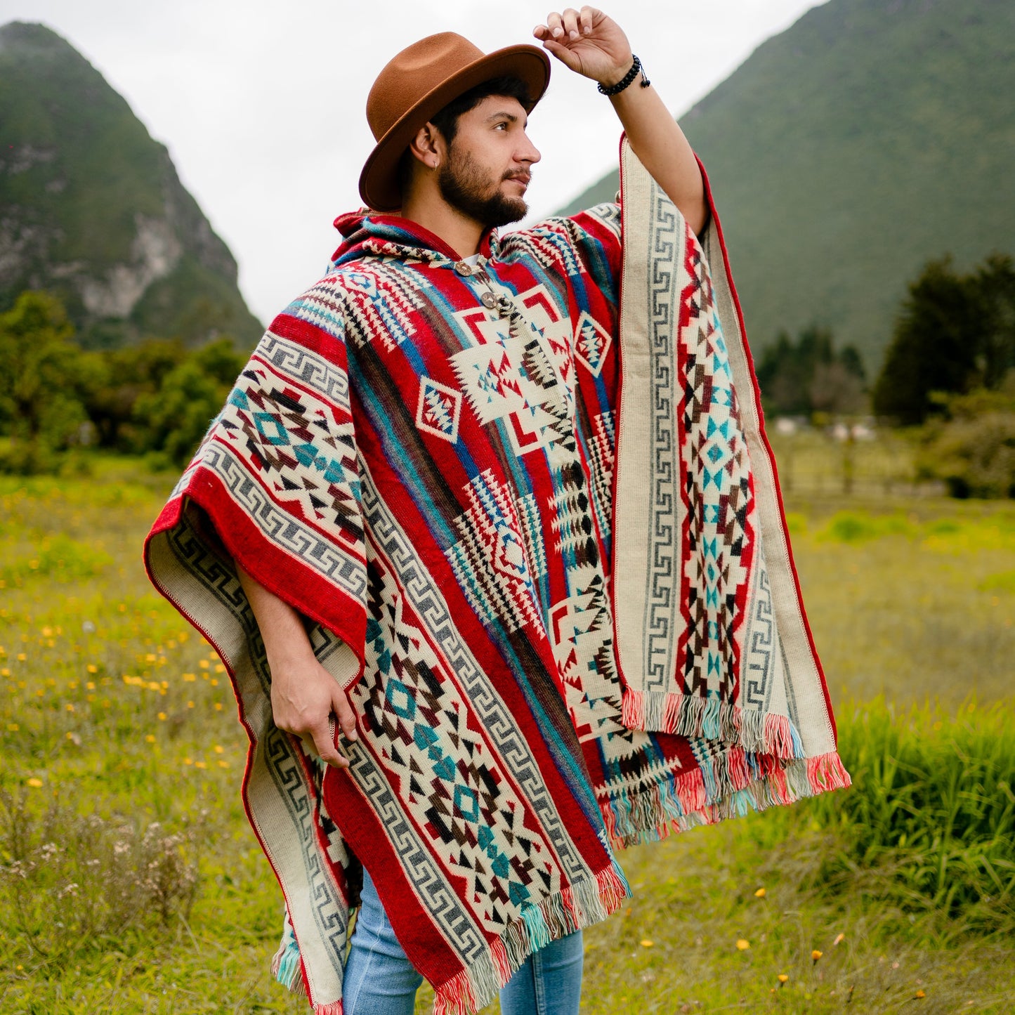 Men’s alpaca wool poncho in red and blue Andean pattern, handmade in Otavalo, Ecuador, with coconut buttons, crafted from 70% alpaca wool and 30% recycled orlon, modeled outdoors in the Andes mountains.
