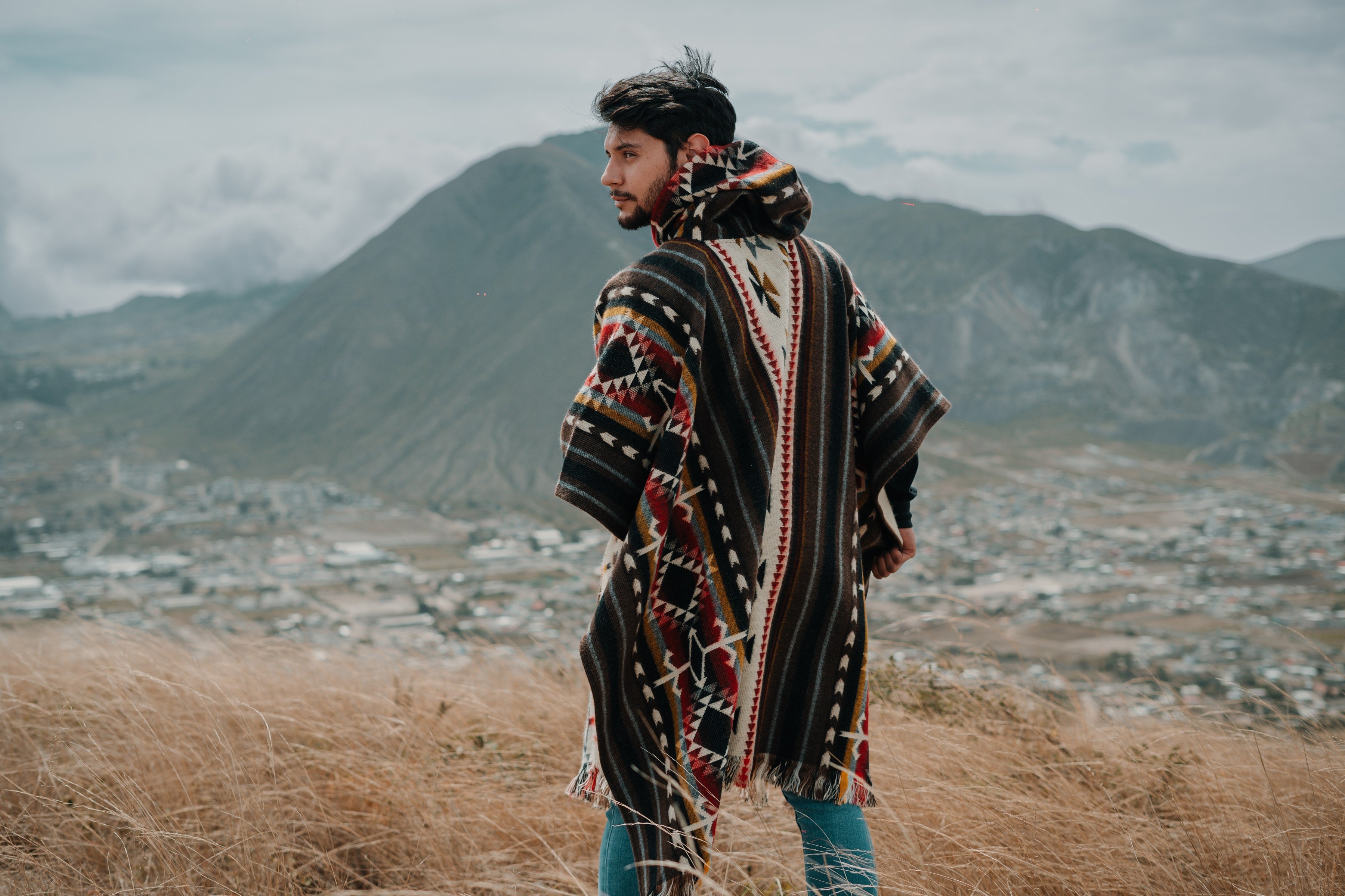 Men's alpaca wool square poncho with Andean heritage design, modeled outdoors in the mountains