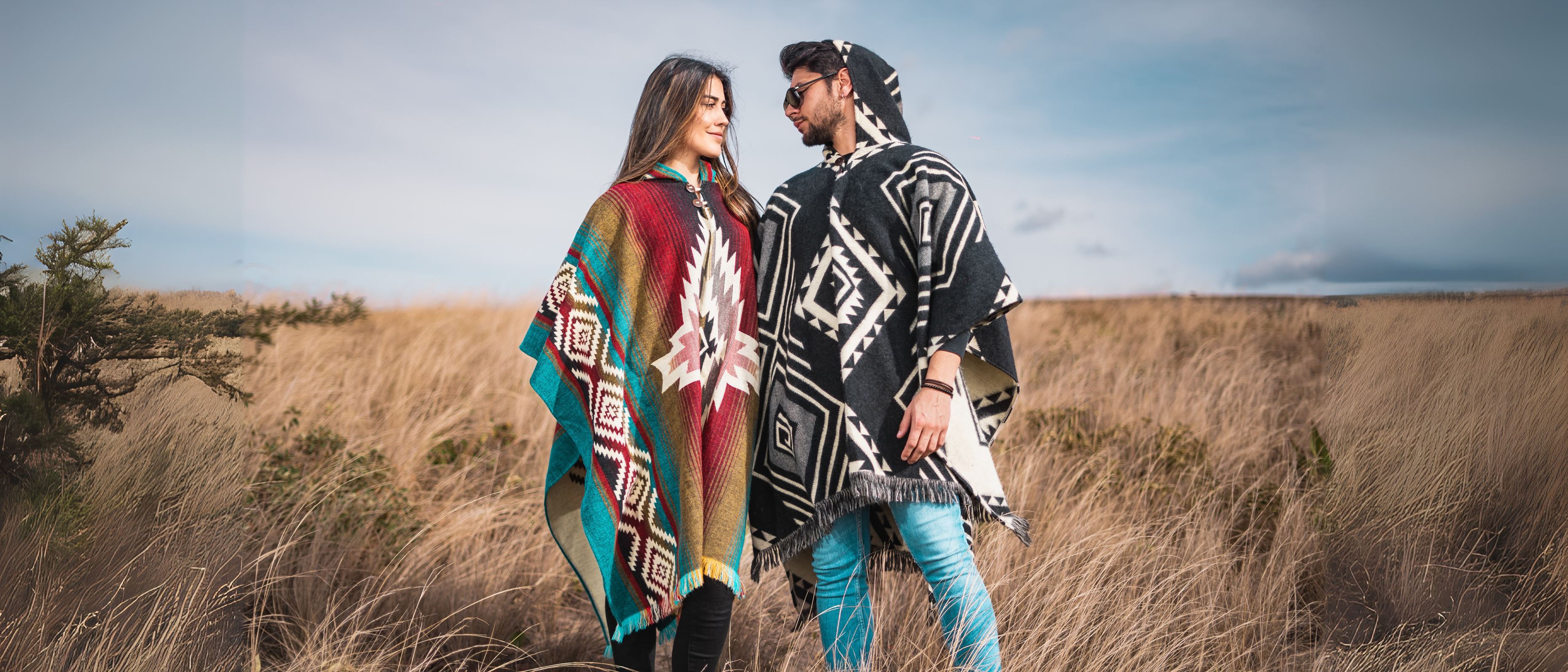 Man and woman wearing colorful authentic alpaca ponchos in a field, handmade in the Andes