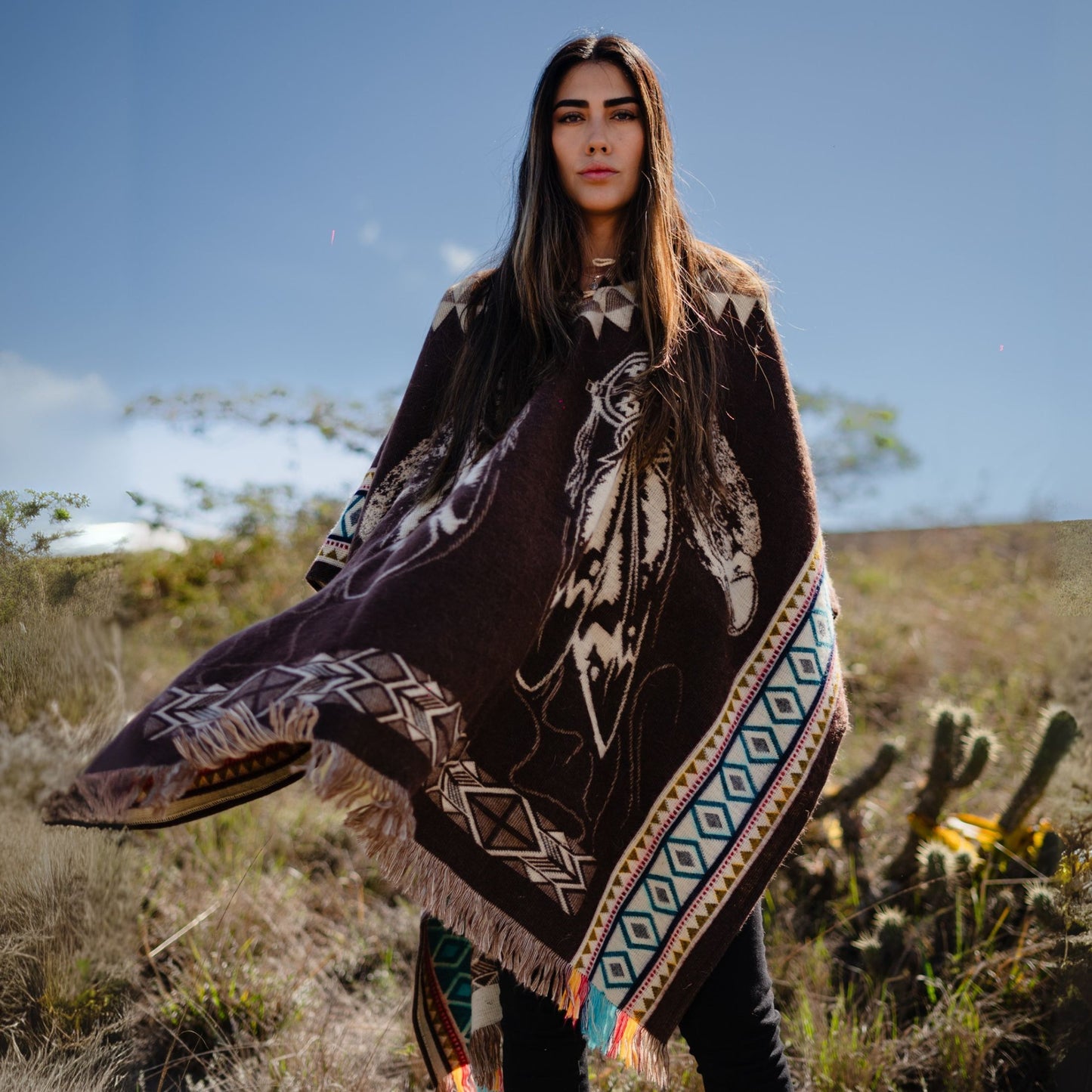 Woman wearing brown alpaca poncho with native Andean design and colorful geometric borders, handmade and sustainable from the Andes.
